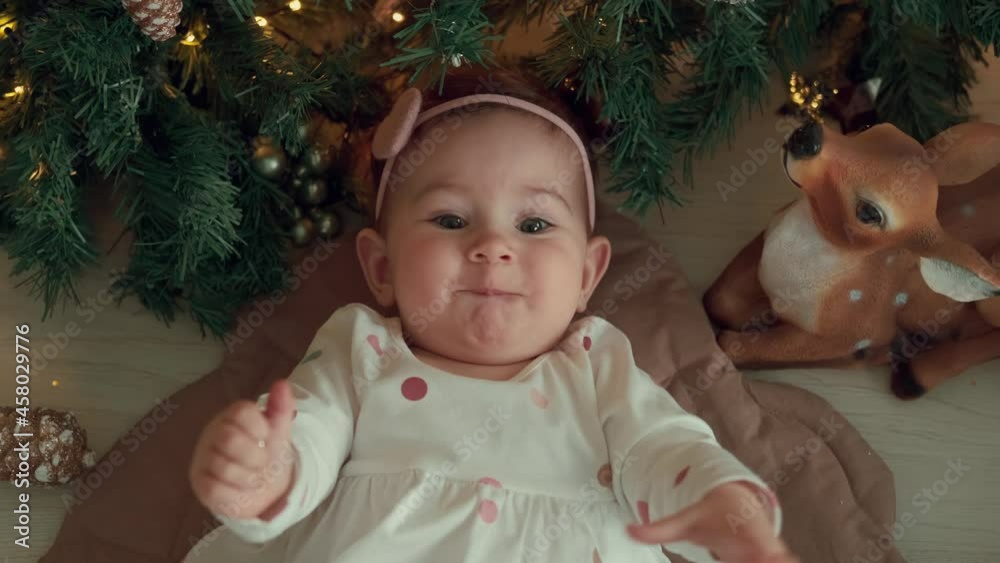 Happy 1 year old child lies near the Christmas tree and laughs.