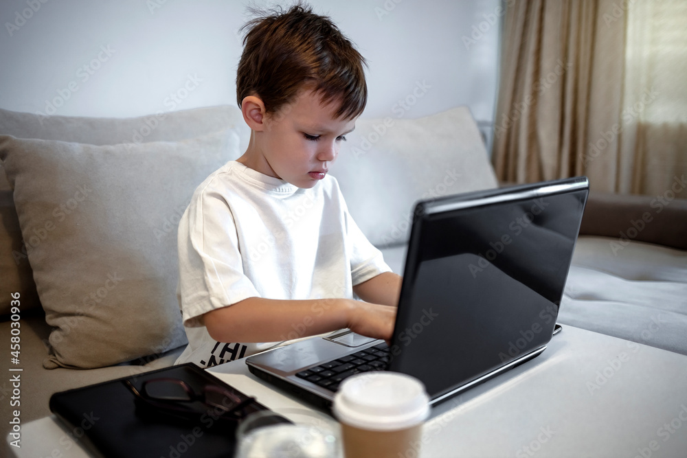 Portrait of teenage Caucasian boy using laptop while studying at home, remote education concept, copy space. Smiling boy looking at laptop. Five years old boy sitting behind a laptop and smiling. Portrait of teenage Caucasian boy using laptop while studying at home, remote education concept, copy space. Smiling boy looking at laptop. Five years old boy sitting behind a laptop and smiling.