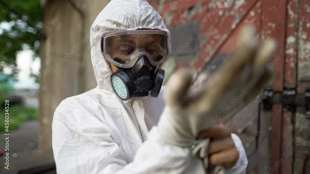 Male worker in protective mask putting on gloves outdoors