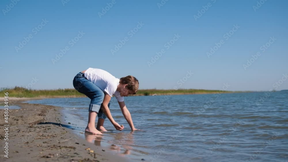 A little boy is having fun alone on the seashore, collecting wet stones in the water. The concept of a fun, peaceful vacation. A little boy is having fun alone on the seashore, collecting wet stones in the water. The concept of a fun, peaceful vacation.