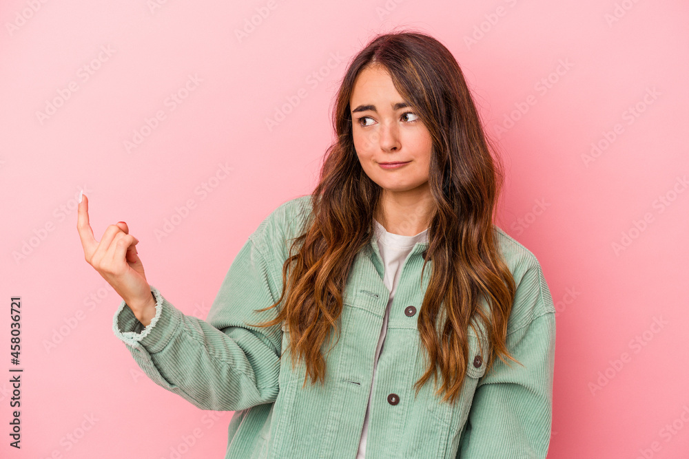 Young caucasian woman isolated on pink background pointing with finger at you as if inviting come closer. Young caucasian woman isolated on pink background pointing with finger at you as if inviting come closer.