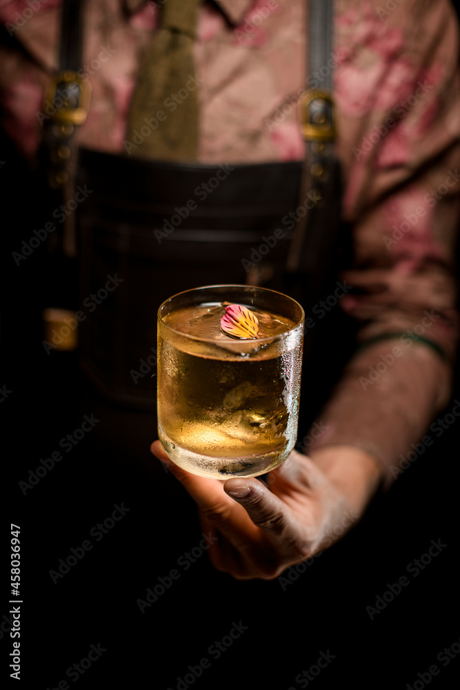 beautiful flower petal decorating cold cocktail in glass gently held by male hand beautiful flower petal decorating cold cocktail in glass gently held by male hand