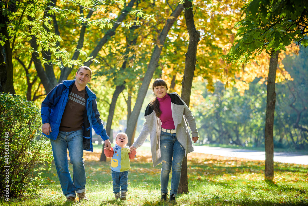 Obraz premium Beautiful young family on a walk in autumn forest on maple yellow trees background. Father and mother hold son on hands. Happy family leisure together concept