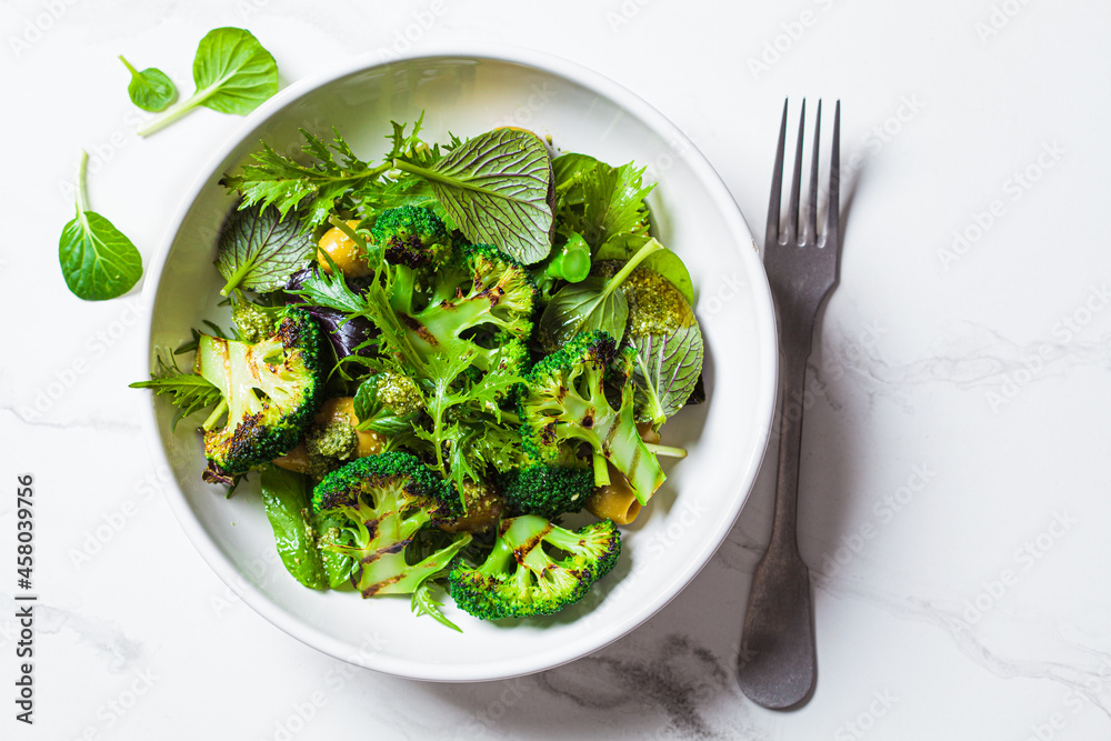 Green salad with grilled broccoli and olives in white bowl. Vegan food, detox, healthy food concept Green salad with grilled broccoli and olives in white bowl. Vegan food, detox, healthy food concept