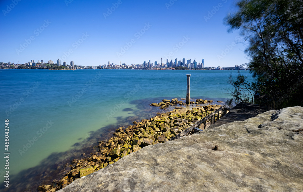 Fototapeta premium Sunny Spring day on Sydney Harbour with nice rocks in the foreground the soft waves crashing on the shore and the beautiful harbour foreshore as a backdrop NSW Australia