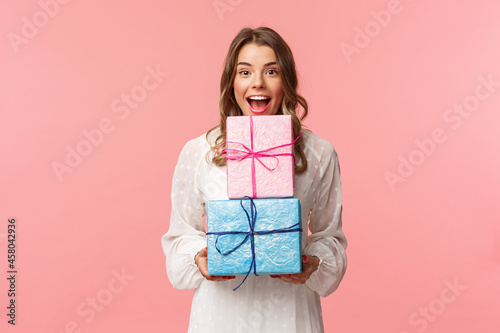 Holidays, celebration and women concept. Portrait of happy cheerful girl likes celebrating birthday and receive presents, holding two gift boxes and smiling camera, pink background photo