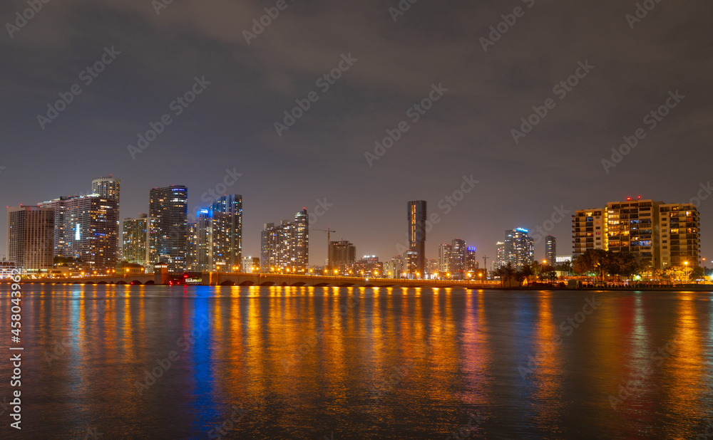 Miami, Florida cityscape skyline on Biscayne Bay. Panorama at dusk with urban skyscrapers and bridge over sea with reflection.