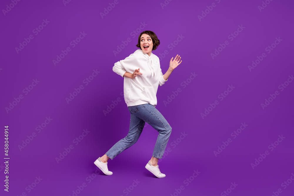 Full size photo of young happy funky girl running away playful wear white sweater isolated on violet color background