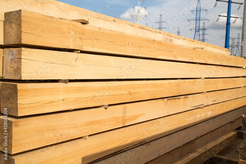 A stack of softwood lumber of yellow color against the blue sky and power lines. Construction production of textures. photo
