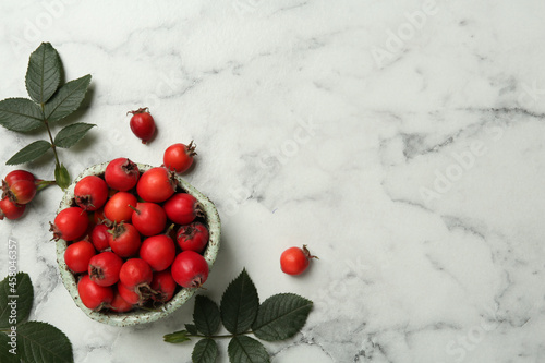Ripe rose hip berries with green leaves on white marble table, flat lay. Space for text