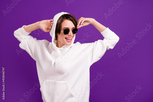 Photo of sweet charming young woman dressed white pullover dark glasses dancing empty space smiling isolated violet color background