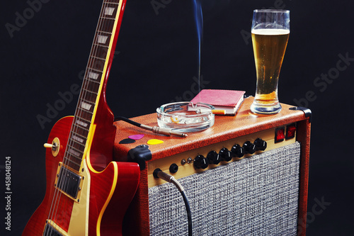 Amplifier for guitar with guitar, glass of beer and smoking cigarette on black background.