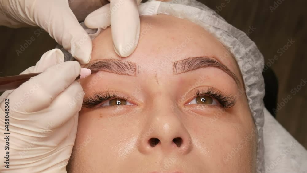 The master draws a new shape of the eyebrows with special pencil in white gloves. Eyebrow shape correction. Microblading, permanent makeup, tattoo