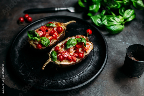 Eggplants with tomatoes, basil and cheese on a black plate