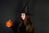 Halloween. Teenage girl dressed as a witch, holding a pumpkin, celebrating Halloween. Copy space. Black background.