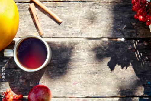 Cup of tea on wooden background in rustic style with trendy natural shadows. Top view, copy space. Viburnum and cinnamon sticks. Autumn aesthetic still life. Thanksgiving Day concept.