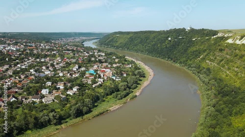 Nature and city landscape. A river with dirty water, a hill with forest and vegetation and a valley with buildings from a bird's eye view. Skyline with blue sky. 4k photo