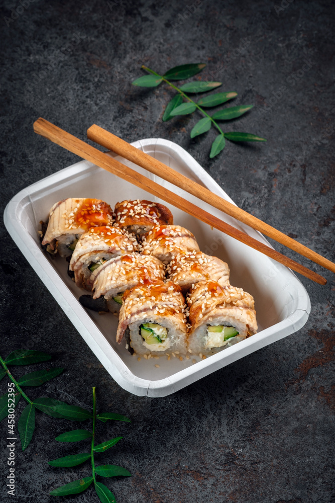 Unagi Philadelphia roll set with cream cheese, cucumber and avocado in a delivery box with chopsticks. Japanese dish with eel fish Unagi Philadelphia roll set with cream cheese, cucumber and avocado in a delivery box with chopsticks. Japanese dish with eel fish