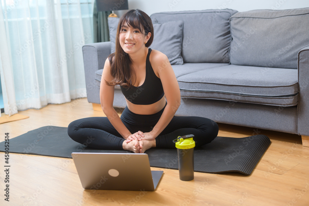 Young woman is exercising and watching online training fitness class on the laptop in living room at home, sport, fitness and technology concept.