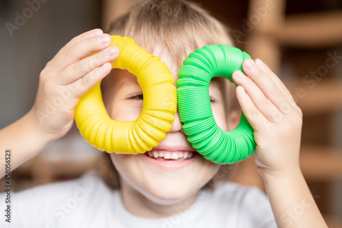 anti stress sensory pop tube plastic toy in kid's hands. a little happy child boy plays with a poptube fidget toy at home. children holding and playing pop tube yellow and green color, trend 2021 year photo