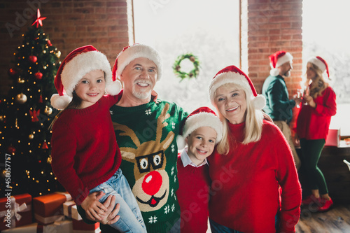 Photo of family friends small childhood grandchildren pensioner retired grandparents noel wear santa claus hat xmas indoors in house