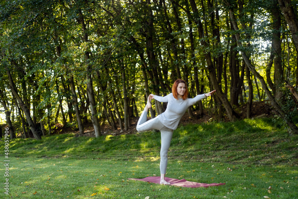 Millennial slim ginger woman doing yoga outdoor on nature in city in autumn sunny day on sunrise Millennial slim ginger woman doing yoga outdoor on nature in city in autumn sunny day on sunrise