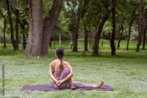 Mexican woman doing yoga exercises in the park on green grass