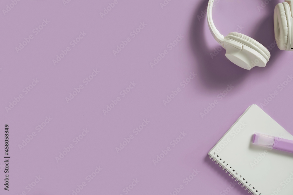 White headphones and notebook with highlights marker flat lay on purple background. Audio sound, music gadgets minimalistic concept.
