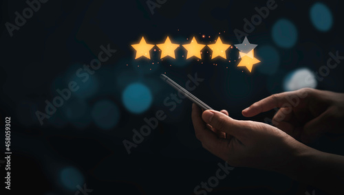 Fotografia Hand holding and using smartphone with virtual five golden stars with glowing light for the best customer client evaluation score after use product and service concept