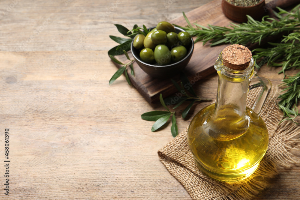 Glass jug of oil, ripe olives and green leaves on wooden table. Space for text Glass jug of oil, ripe olives and green leaves on wooden table. Space for text
