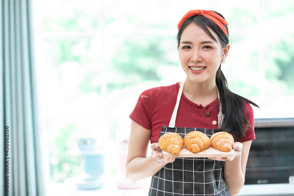 young woman housewife holding fresh croissants on the cutting board, for enjoy eating in the kitchen