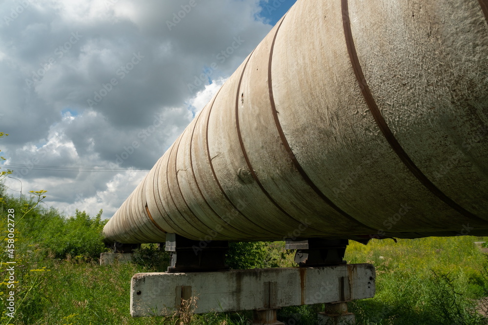 A section of the pipeline of the ground heating main of the main heating network on a reinforced concrete support among the grass on a sunny summer day. A section of the pipeline of the ground heating main of the main heating network on a reinforced concrete support among the grass on a sunny summer day.