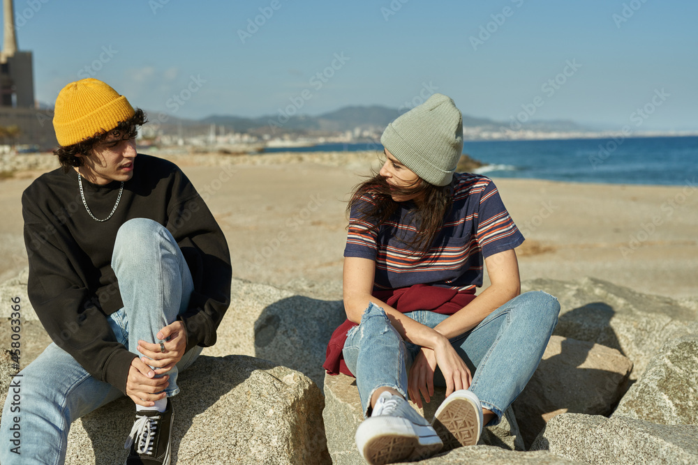Two riveted young people sitting on rocks - obrazy, fototapety, plakaty 