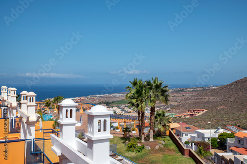 Clear sunny summer views towards Costa Adeje from the hills high above  exhibiting properties and residential areas  tropical trees and ample Atlantic Ocean vistas in Tenerife  Canary Islands  Spain