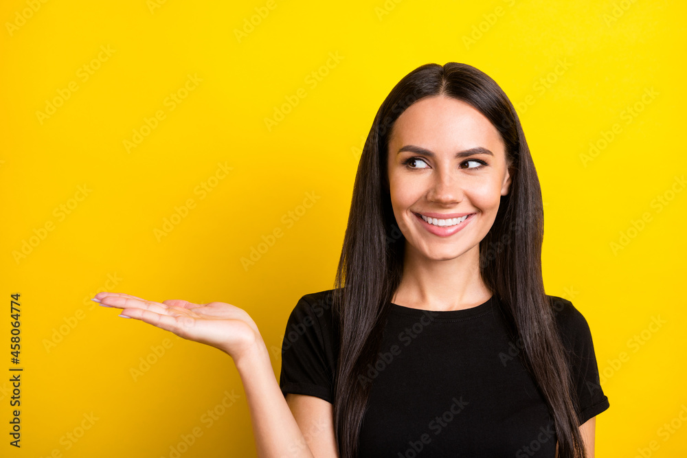 Portrait of charming positive person look interested hand palm hold empty space isolated on yellow color background Portrait of charming positive person look interested hand palm hold empty space isolated on yellow color background