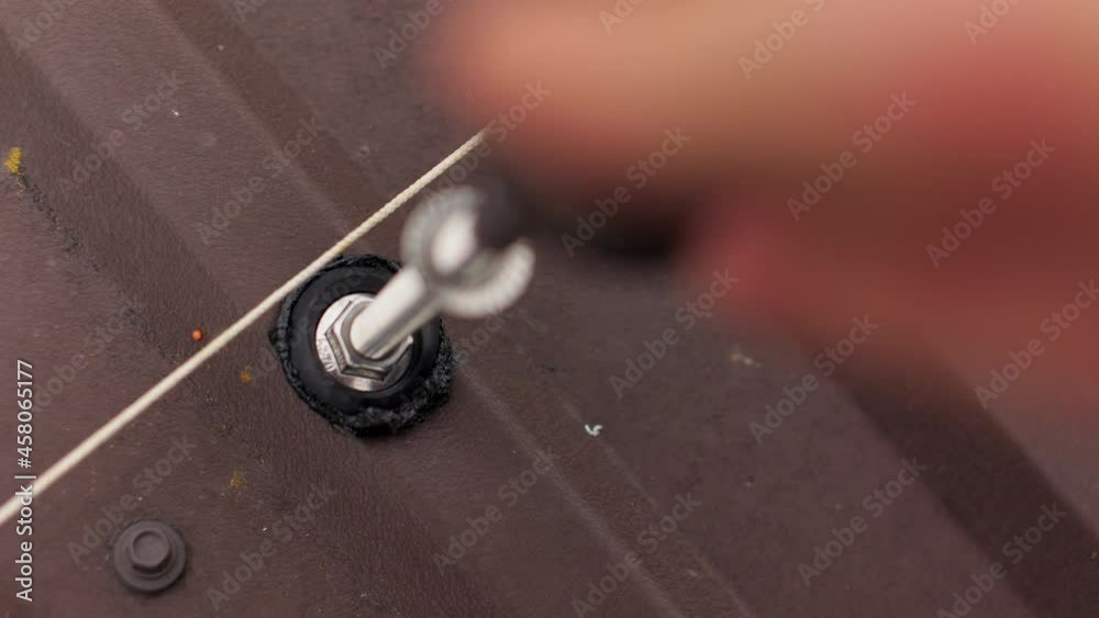 Close up of a screw with a sealant with an electric screwdriver in the roof. Installation of fastenings on a roof Close up of a screw with a sealant with an electric screwdriver in the roof. Installation of fastenings on a roof