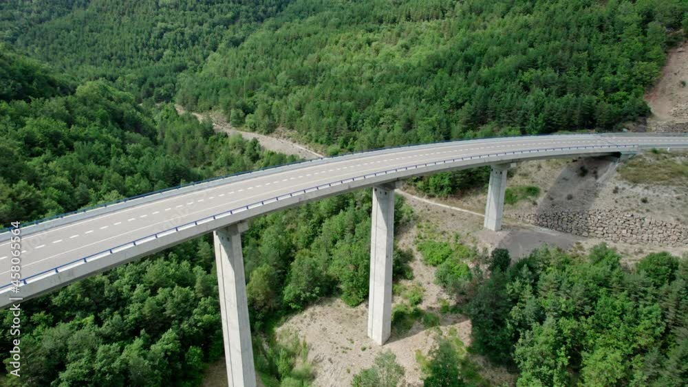 A bridge, a modern viaduct in the mountains with an asphalt road with three lanes. Reinforced concrete wharf structure of the bridge connecting two hills in the mountains covered with forests. A bridge, a modern viaduct in the mountains with an asphalt road with three lanes. Reinforced concrete wharf structure of the bridge connecting two hills in the mountains covered with forests.