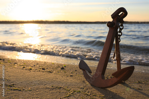 Canvas-taulu Wooden anchor on shore near river at sunset