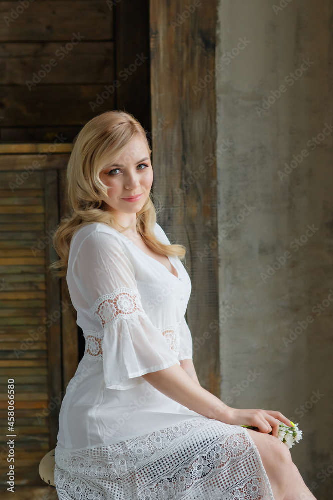 Fototapeta premium Boudoir photo of the bride in the morning. A beautiful portrait of a young blonde woman in a white coat sitting by the window.