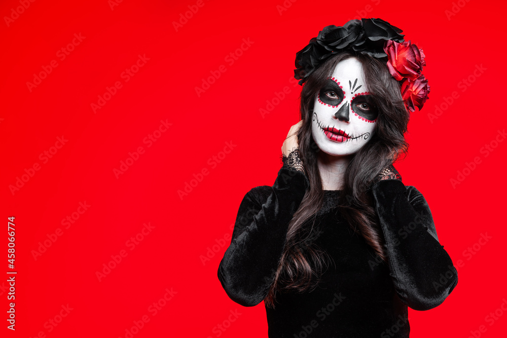 Girl with creative sugar skull makeup with a wreath of flowers on head, wide isolated on red background. Holiday concept Dia De Los Muertos on poster for Halloween party or La Calavera Catrina. Girl with creative sugar skull makeup with a wreath of flowers on head, wide isolated on red background. Holiday concept Dia De Los Muertos on poster for Halloween party or La Calavera Catrina.
