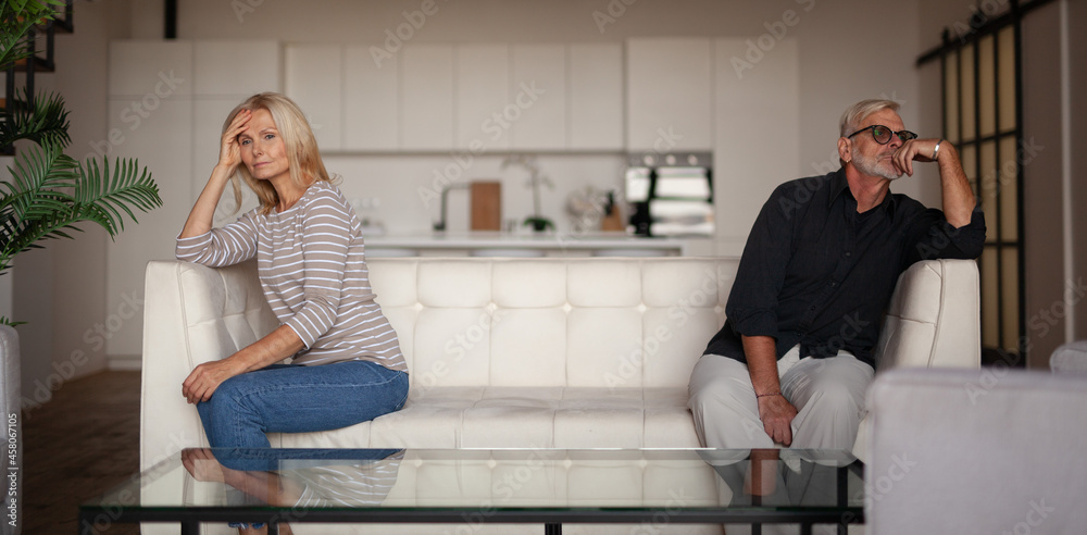 Quarrel and conflict in a mature family. Upset husband and wife are sitting on opposite sides of the sofa. Problems in the relationship between a man and a woman. Quarrel and conflict in a mature family. Upset husband and wife are sitting on opposite sides of the sofa. Problems in the relationship between a man and a woman.