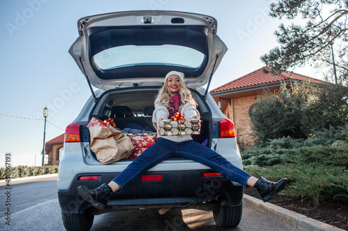 The girl is smiling and sit in the trunk of the car with x-mas boxes. the New Year's mood. Beautiful woman dressed sweater and jeans preparing for Christmas or New year's eve celebrations, buys gifts 