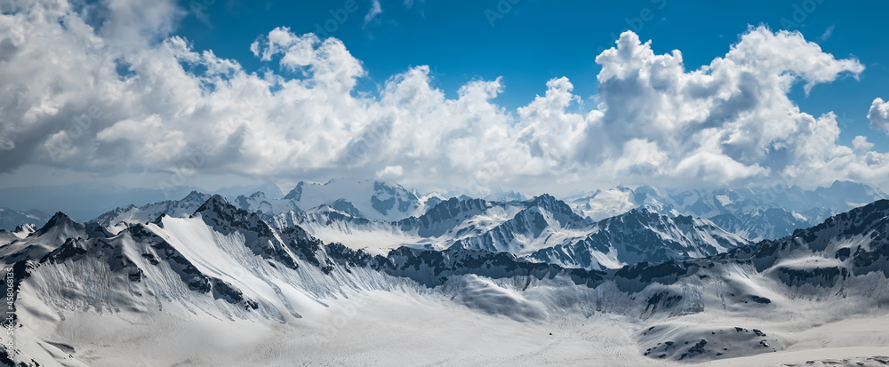 Mountain clouds over beautiful snow-capped peaks of mountains and glaciers. View at the snowy mountains.