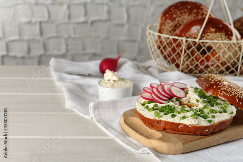 Delicious bagel with cream cheese, radish and green onion on white wooden table. Space for text