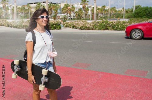 A middle-aged woman in sunglasses enjoying skateboarding in the street.