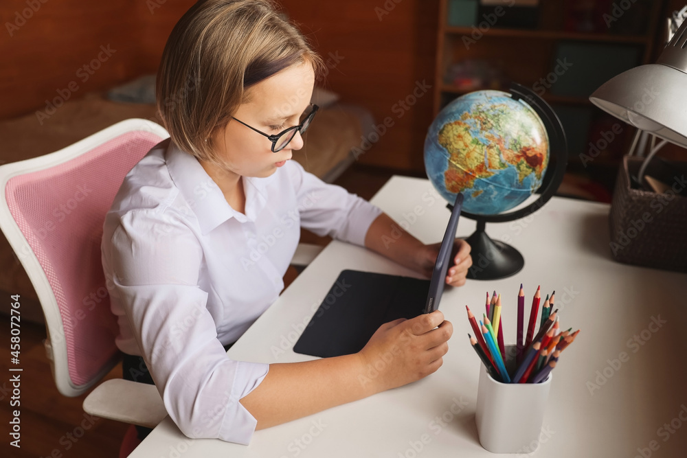 Fototapeta premium Schoolgirl engaged in homeschooling, watching online learning lecture on laptop at home. Kid attending remote virtual school class, listening to teacher. Remote learning at home with technology