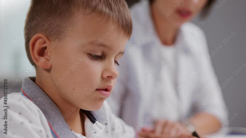 Cute caucasian boy sitting with his charming mother at desk and drawing with colorful pencils in album. Family spending time with education and creativity at home Cute caucasian boy sitting with his charming mother at desk and drawing with colorful pencils in album. Family spending time with education and creativity at home
