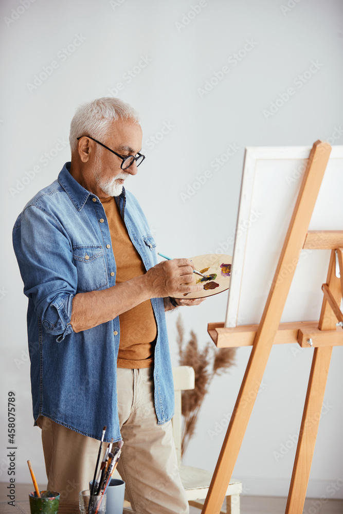 Fototapeta premium Senior artist enjoys while painting on canvas at his home studio.