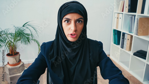 displeased arabian businesswoman in hijab looking at camera in office photo