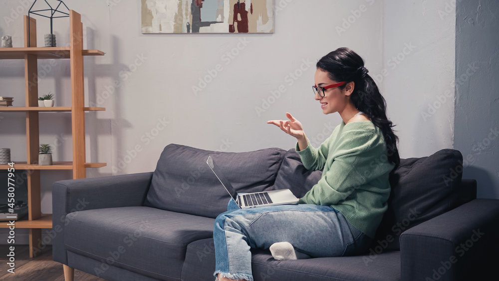 Obraz premium Side view of smiling freelancer having video call on laptop on couch